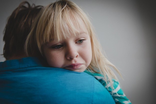 alt="Worried young girl resting on parent's shoulder, possibly experiencing discomfort or concern related to scoliosis"
