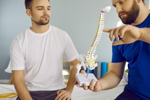 Chiropractor explaining spine anatomy using a model while male patient listens attentively during consultation.